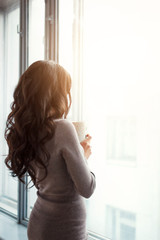 beautiful slender girl by the window with a cup of coffee in her