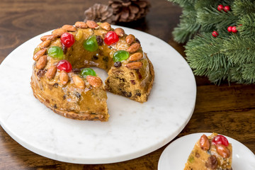 Colorful Christmas fruitcake topped with almonds and glace cherries on white platter