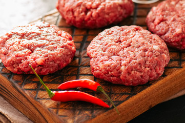 Close up of raw ground meat beef burgers on a wooden board.