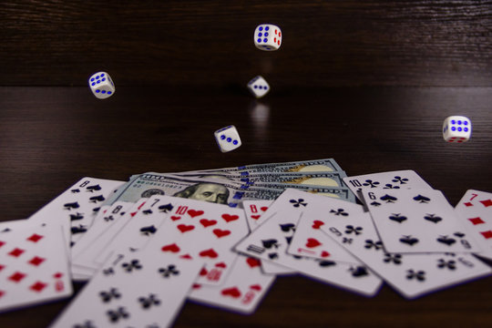 Dice in a flight above the one hundred dollar bills and playing cards. Gamble concept