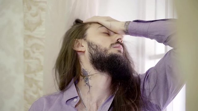 Male model with a long hair and a beard is in a luxury apartment.