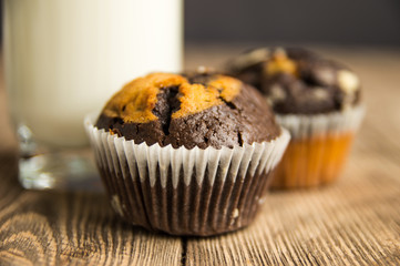 Two chocolate cupcakes and a glass of milk on a wooden table