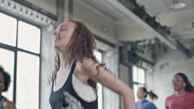 Medium shot with low angle of curly young woman jumping and doing aerobics in group class