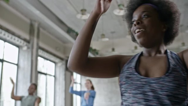 PAN of energetic instructor with curly hair and African woman dancing zumba in group class