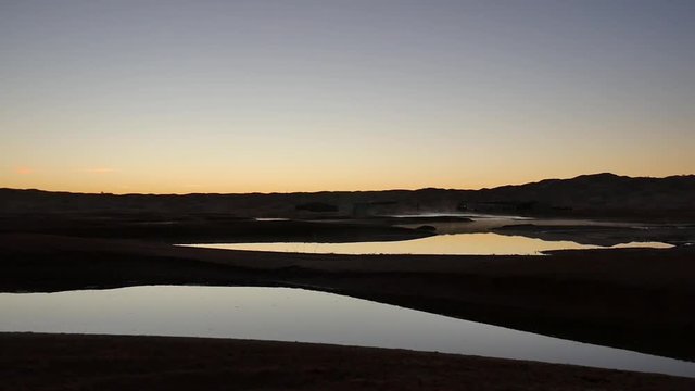 Un esploratore osserva l'alba nel deserto di fronte ad una oasi del Sahara