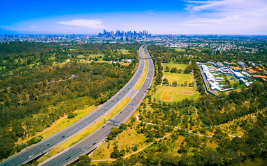 Aerial panorama of green parkland, Melbourne Polytechnic, and Melbourne CBD skyscrapers in the distance on summer day