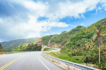 Road crossing the forest with cloudy sky and mountain view.