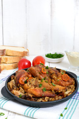 Pieces of fried rabbit with forest mushrooms on a cast-iron frying pan on a white wooden background.