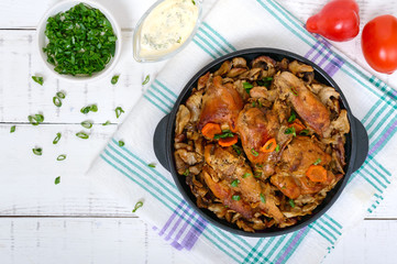 Pieces of fried rabbit with forest mushrooms on a cast-iron frying pan on a white wooden background.