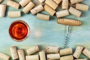 Wine glass, corkscrew, and corks on teal background with copy space