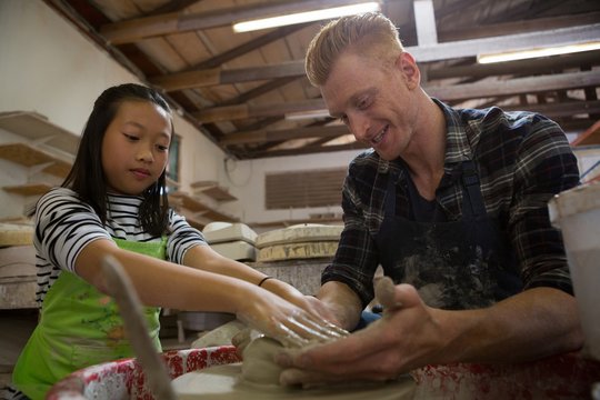 Male potter assisting his daughter in making a pot
