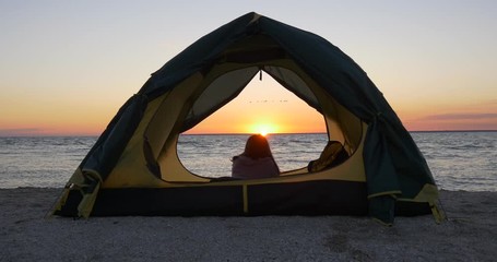 Girl meets sunrise on the beach in a tent