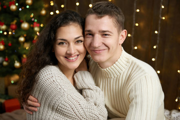 couple in christmas lights and decoration, dressed in white, young girl and man, fir tree on dark wooden background, winter holiday concept