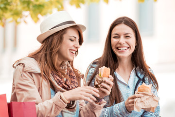 Two beautiful girls eating sandwiches after shopping.