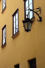 Fototapeta na wymiar Street lamp (lantern) with forged metal elements on ancient building with narrow windows. Old facade house. Old town european street. Antique architecture.