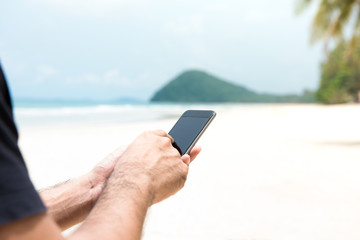 Male tourist using smartphone on the island at the beach in summer vacation