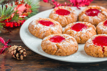 Traditional German Christmas cookies Engelsaugen with red berry jam on a white plate on the wooden table