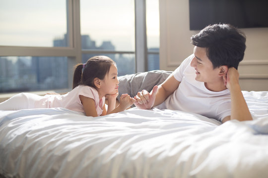 Cheerful young father making a pinky swear with his daughter on bed