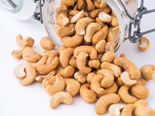 Glass bottle with cashew nuts on white background. A glass bowl with a scattering of nuts, side view,