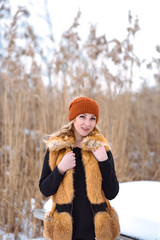 beautiful girl in a fur vest walks in a field in the snow