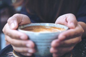 Closeup image of hands holding a cup of hot coffee on glass table in cafe