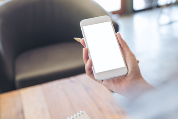 Mockup image of a hand holding white mobile phone with blank screen and a pen in office