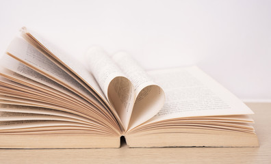 Page of book curved into heart shape on wood table. valentine concept.