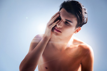 Obraz premium Sensitive touch. Pleasant nice young man standing against bright background and touching his face while being thoughtful