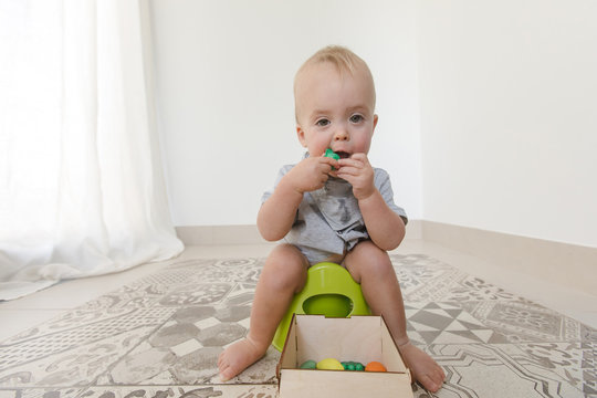 Baby sitting on potty and eating vegetables at home interior