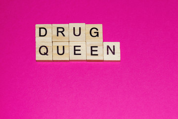 Wooden blocks on a pink background spelling words Drug Queen