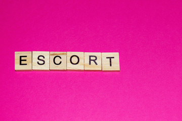 Wooden blocks on a pink background spelling word Escort