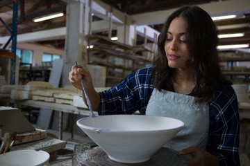 Female potter decorating bowl with paint brush