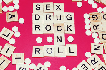 Wooden blocks on a red background spelling words Sex Drug Rock n Roll surrounded by tablets