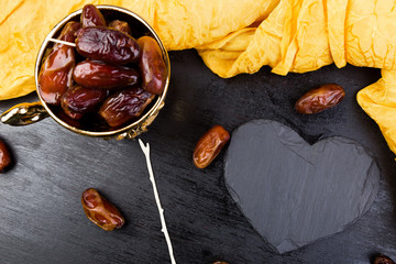 Dry fruit dates in golden cup near slate black heart. Copy space.Valentine Day.