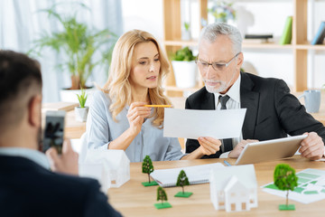 Look here. Clever skilled reliable worker looking concentrated while sitting with her older colleague and showing him an important part of a document