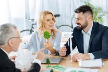 Lovely trees. Creative enthusiastic young engineer feeling glad while showing a nice model of a tiny tree to her colleagues and persuading them to include it into their project