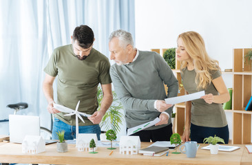 Busy people. Smart responsible attentive engineers looking concentrated while standing round the table with schemes in their hands and working at the significant ecological project