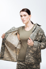 Combat uniform. Serious pensive confident woman touching military jacket while posing on the white background and looking at the camera
