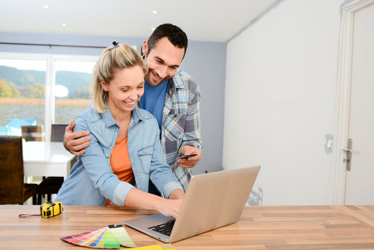 cheerful young couple renovating home design and choosing colors paint and furnitures on internet with a laptop computer