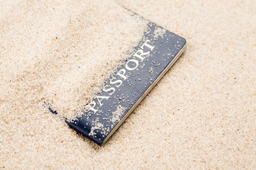 Blue passport covered with sand on a beach