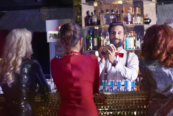 Rear view of bartender preparing cocktail for pretty women