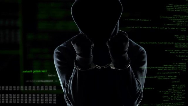 Male hacker with handcuffs standing in front of animated computer code, IT thief