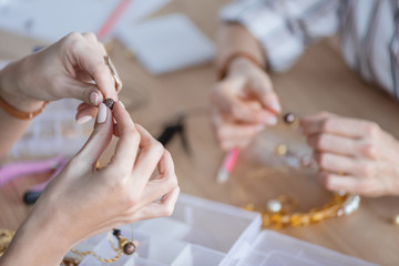 cropped shot of women making accessories of beads at workshop