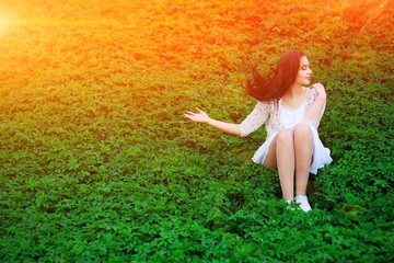 brunette woman in dress sitting on the grass and waving in the wind their hair with her hand