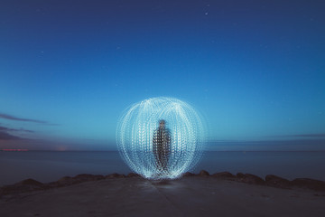 Person creating light ball at seashore at night 
