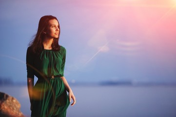 beautiful woman in a green dress looks at the evening sun.