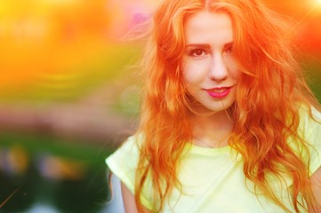 A wonderful portrait of a beautiful young woman with red hair and bright makeup outdoors in the summer.