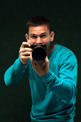 Portrait of positive male photographer holding digital camera and preparing to make a shoot, posing over green background
