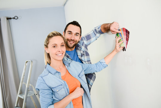 cheerful young couple choosing wall paint color for their new home decoration