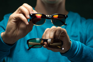 Closeup man wearing casual clothes holding two stylish eyeglasses in hands.